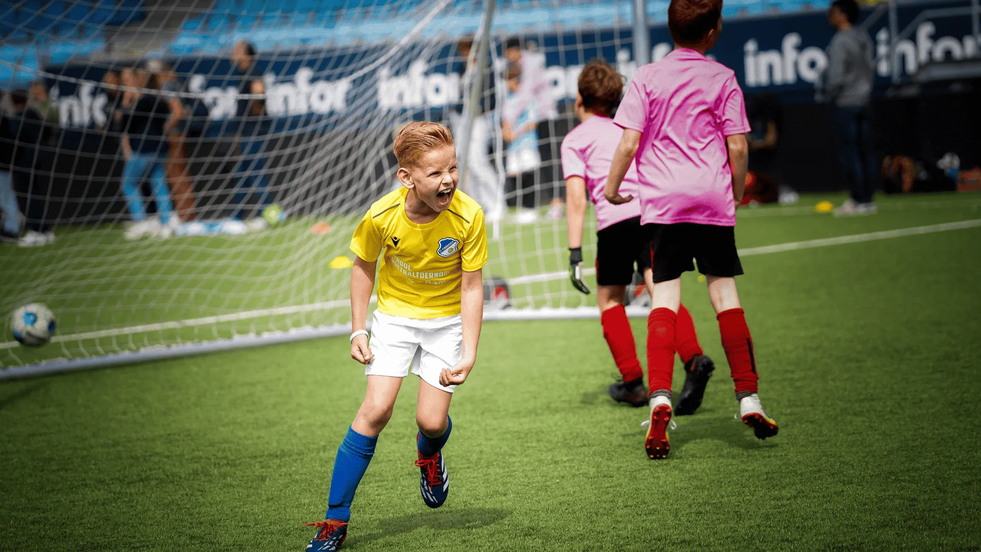 Juichende basisschoolspeler in geel toernooishirt bij het ASML Schoolvoetbaltoernooi