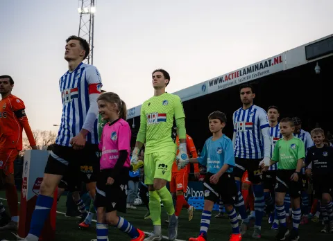 Kinderen in ASML Schoolvoetbaltoernooi-shirts lopen met de spelers het veld op